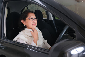 Indonesian moslem woman sitting wondering in her seat behind car steering wheel