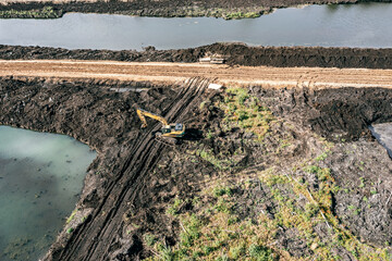 large yellow backhoe digs a reclamation ditch. land improvement. aerial drone photo.