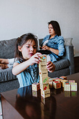 Latin girl child daughter playing with bricks at home in Mexico with family on background, Hispanic people
