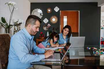 Latin Family father and mother working from home using laptop while take care of daughter and son...