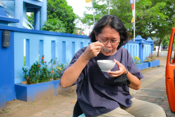 A woman is taking a break and enjoying a bowl of Javanese traditional dessert.