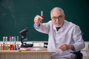 Old male chemist teacher sitting in the classroom