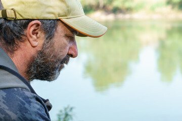 close-up of a fisherman with beard and cap seen in profile on the river bank