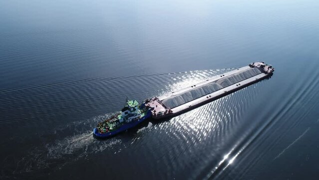 Aerial view. The barge floats on a wide river loaded with rubble. The bulk carrier transports gravel on a navigable river.  Delivery of raw materials by water.  View from drone.