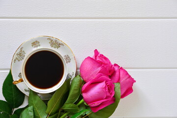 Beautiful festive morning breakfast. Porcelain pattern cups of black coffee on saucer and bouquet of red roses on white background. Copy space, top view