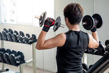 Sport man with well trained body in black sportswear doing seated dumbbell shoulder press on workout bench in fitness gym. Weight training and bodybuilding workout concept.
