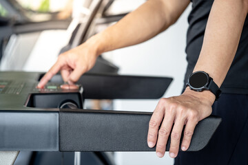 Runner man wearing smartwatch while using treadmill running in fitness gym. Wearable device for sport activity. Smart watch technology for health tracking. Healthy lifestyle concept.