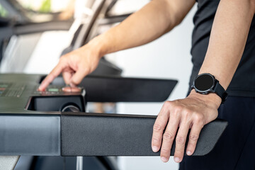 Naklejka premium Runner man wearing smartwatch while using treadmill running in fitness gym. Wearable device for sport activity. Smart watch technology for health tracking. Healthy lifestyle concept.