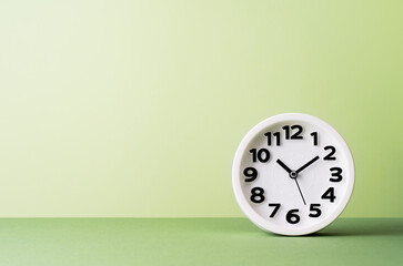 Plain white clock on pastel green background desk. Ten o'clock. copy space, time management or...