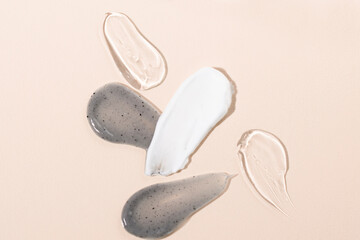 Smears of cosmetic textures on a beige background top view. Charcoal face mask, body cream, gel, serum macro samples.