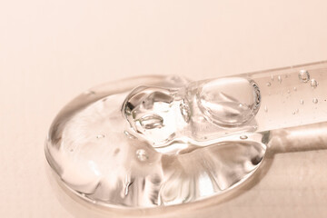 Liquid transparent texture of a beauty product on a beige background with a dropper close-up. Facial moisturizer, aloe vera gel.