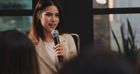 Confident young businesswoman or speaker sharing ideas with colleagues or audience during company seminar.