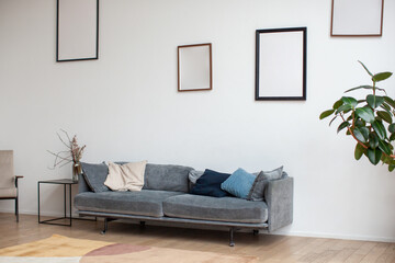 Empty picture frame mockup on white wall. Modern interior with sofa. Cozy home. 
