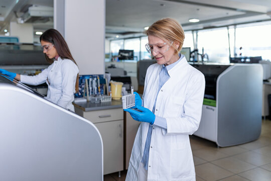 Female Research Scientist Putting Test Tubes with Blood Samples into Analyzer Medical Machine. Scientist Works with Modern Medical Equipment in Pharmaceutical Laboratory.