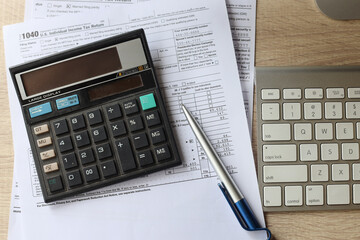 Overhead view of work desk with keyboard, calculator, pen and income tax return form. 