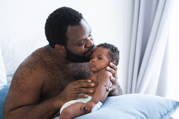 African American bearded father kissing and lull cute newborn baby in his arms and hand at bedroom at home, infant boy 2 months old lying on pillow, African American family and newborn care concept