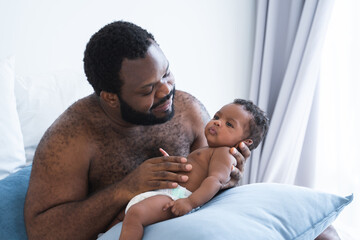 African American bearded father smiling and lull cute newborn baby in his arms and hand at bedroom at home, infant boy 2 months old lying on pillow, African American family and newborn care concept