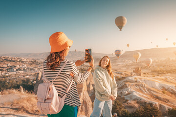 Two happy girl friends taking photos and video on phone for social networks in Cappadocia, Turkey....