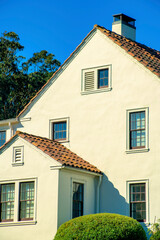 White timber house facade with wooden exterior and gray red roof tiles and visible windows and chimney vents