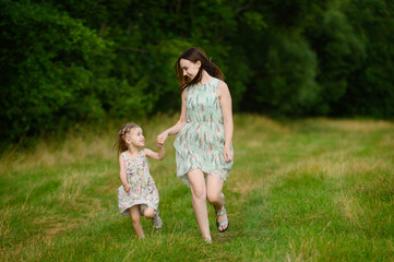 Fototapeta premium Portraits of joyful mother and daughter spend time together, enjoy happy family time, run in the park. Mother's day.