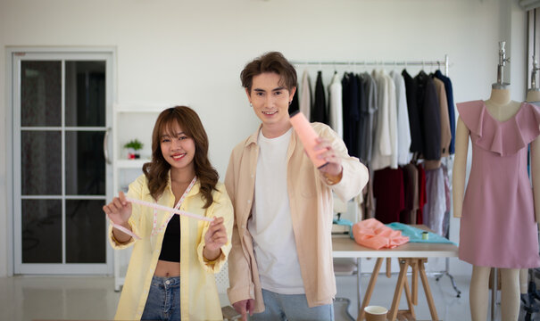 Two adult clothing designers collaborate in a design studio while holding a measuring tape and sewing thread. An image of  entrepreneurs in the fast fashion industry