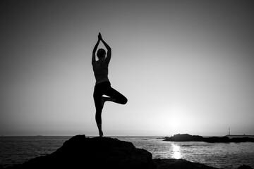 Yoga woman meditating on the rocks of the Atlantic Ocean. Black and white photo.