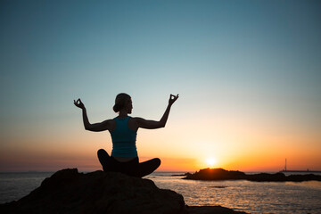 Silhouette of a middle-aged yoga woman on the ocean, during sunset.