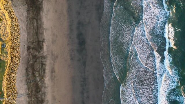 Stationary Vertical Aerial Shot Looking Straight down at Pacific Ocean Beach at Rockaway Beach, Oregon, Pacific Northwest, with Incoming Waves and an RC Car Making Tracks in a Strip of Magnetite