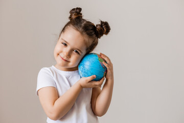 a happy little girl is holding a small globe planet in her hands in a white T-shirt on a white background. Earth Day, space for text