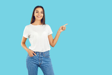 Happy beautiful young brunette woman wearing casual white Tshirt and blue jeans standing isolated on blue background and pointing sideways to show something on blank empty advertising copy space side