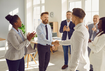 Fototapeta Happy professional business teams making a deal, showing recognition to each other's hard work, and exchanging handshakes. Two men shake hands while their joyful diverse colleagues are applauding obraz