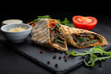 Shawarma with meat, cheese, tomatoes and sauce, on a black background