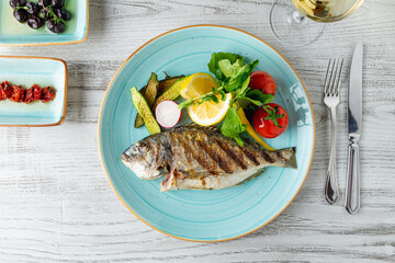 Grilled sea bream with vegetables and greens on wooden table