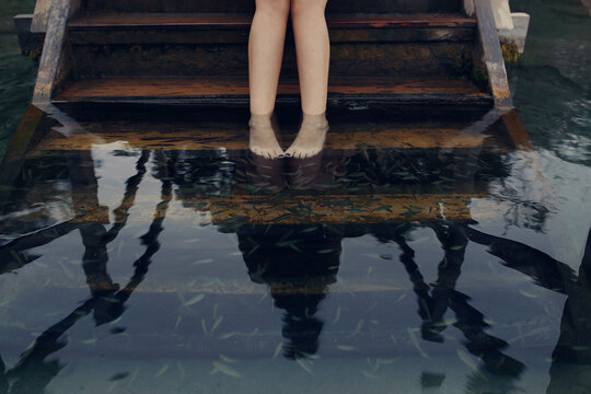 Low section of woman taking fish pedicure while standing on steps in lake
