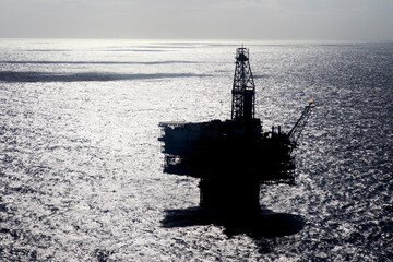 Silhouette oil platform in sea on sunny day