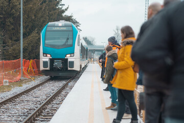 Modern train arriving to the station of Domzale which is being renovated and modernized. People waiting on a temporary platform on a dull day.