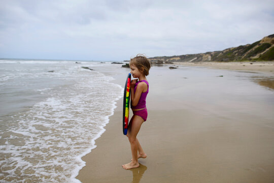 Side view of girl holding surfboard while standing at beach on Crystal Cove State Park against sky