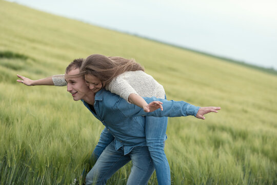 Cheerful couple with arms outstretched enjoying piggyback ride on grass field against sky