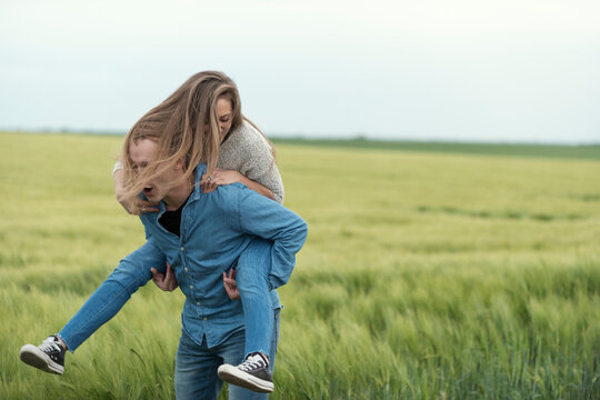 Cheerful man piggybacking woman on grassy field against sky