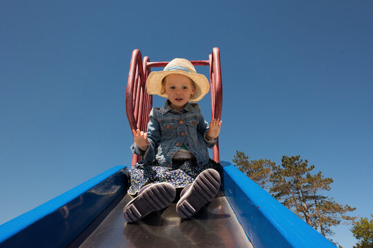Low angle view od cute girl playing on slide at playground against clear sky