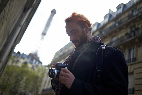 Low angle view of man watching pictures on DSLR camera against Eiffel Tower and buildings