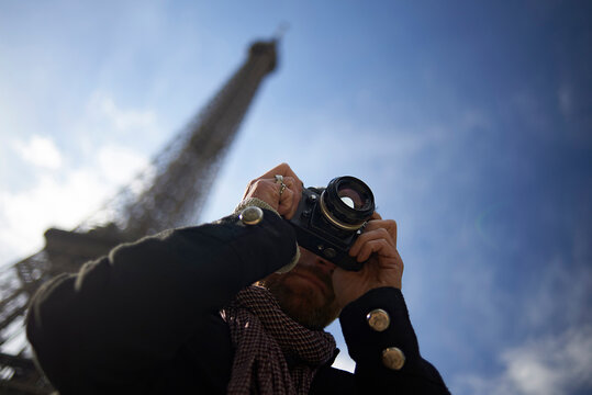 Low angle view of man photographing through DSLR camera against Eiffel Tower and blue sky