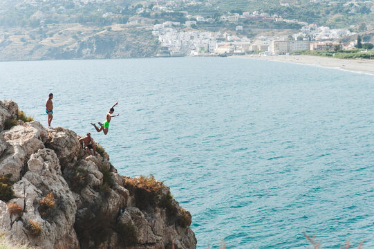 Friends looking at man jumping into sea from cliff