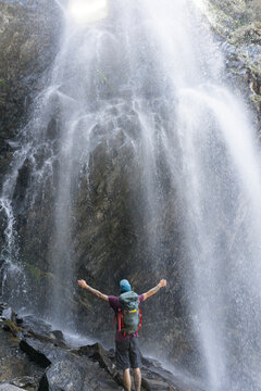 Rear view of hiker with arms outstretched standing against waterfall