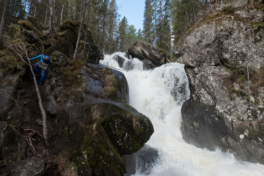 Rear view of female hiker climbing on rock formations by waterfall in forest