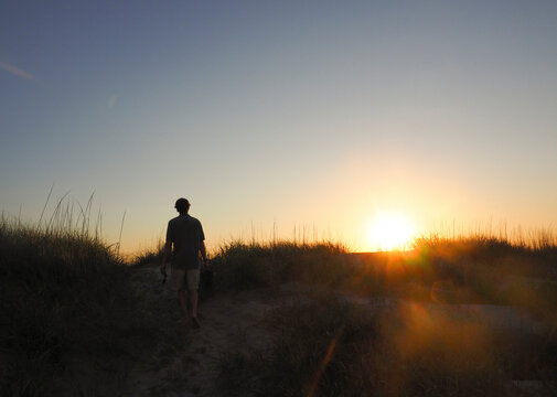 Rear view of hiker walking on field at Nags Head against clear sky during sunset