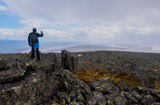Rear view of hiker photographing while standing on mountain cliff against cloudy sky
