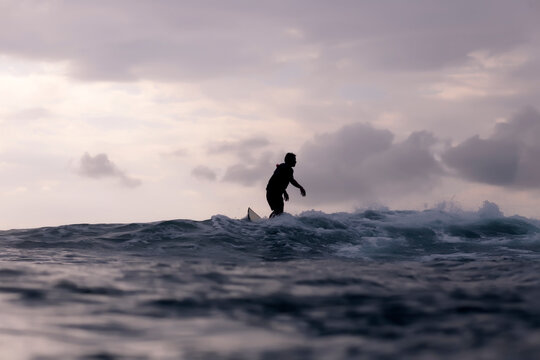 Silhouette man surfing in sea against cloudy sky