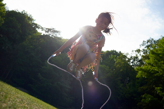 Low angle view of girl jumping rope at park against sky during summer