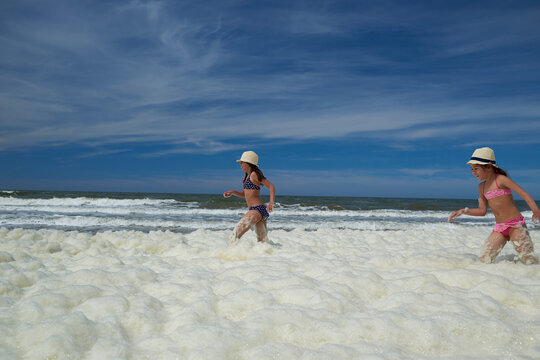 Sisters playing in sea foam at beach against sky